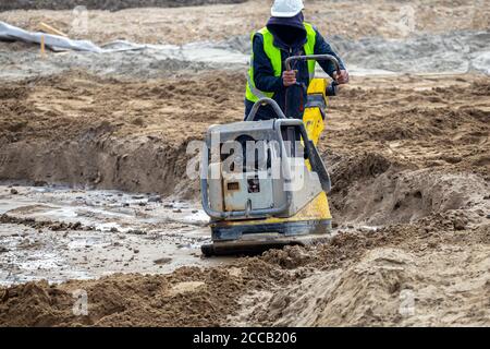 Derrière la machine vibrante se trouve le compactage du sol sur le chantier de construction. Banque D'Images