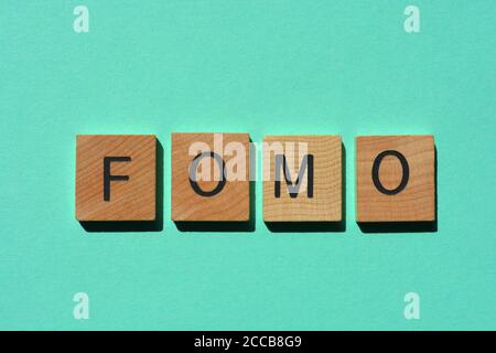 fomo, acronyme de Fear of Missing Out en lettres de l'alphabet en bois isolées sur fond tyrquoise Banque D'Images