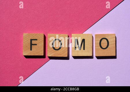 fomo, acronyme de Fear of Missing Out, en lettres de l'alphabet en bois 3D isolées sur fond rose et violet Banque D'Images