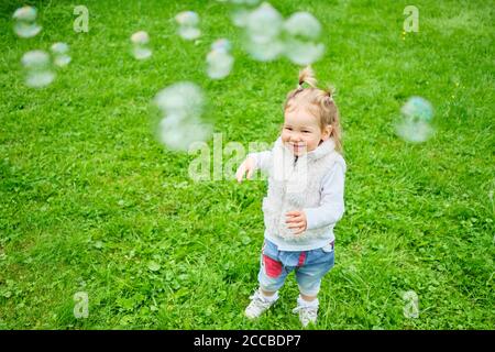 Un tout-petit heureux pourchassant les bulles de savon dans un parc d'été Banque D'Images