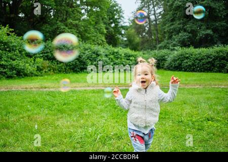 Un jeune enfant souriant chassant les bulles de savon dans un parc d'été. Banque D'Images