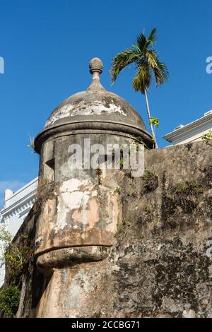 Une ancienne boîte de sentry espagnole sur le mur de la ville du vieux San Juan, Porto Rico avec une architecture plus moderne et un palmier derrière. Banque D'Images