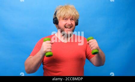 Drôle d'homme gras avec des haltères faisant des exercices sur un fond bleu. Banque D'Images