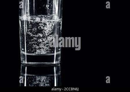 Verser de l'eau minérale dans le verre sur fond noir. Gros plan extrême Banque D'Images