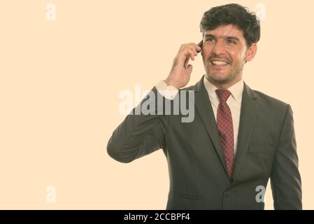 Young happy Persian businessman smiling while talking on mobile phone, portrait Banque D'Images