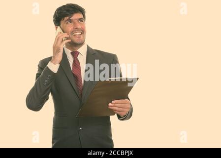Persan heureux réfléchis businessman smiling and holding clipboard while talking on mobile phone Banque D'Images