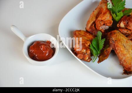 assiette d'ailes de poulet sur la sauce rouge de table blanche dans un saucière Banque D'Images