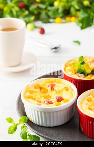 Délicieux clafoutis à base de yaourt blanc et de baies, dessert de prune cerise dans des bols en forme de porc sur la table avec une tasse de jus Banque D'Images