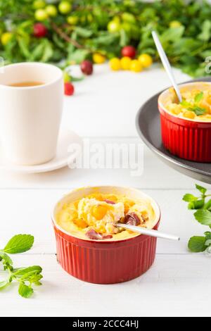 Délicieux clafoutis à base de yaourt blanc et de baies, dessert de prune cerise dans des bols en forme de porc sur la table avec une tasse de jus Banque D'Images