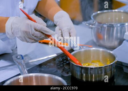 Chef remuant les légumes à la main avec une cuillère dans une casserole sur cuisinière électrique à la cuisine du restaurant. Cuisine professionnelle, restauration, cuisine, gastronomie et Banque D'Images