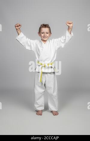 portrait d'un enfant portant un kimono d'arts martiaux debout souriant et dans une position gagnante. Banque D'Images