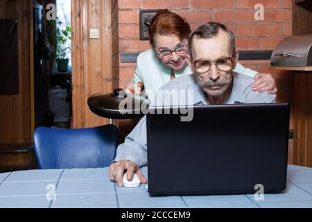 Problèmes familiaux dus à l'ordinateur. Un couple âgé dans la cuisine, un homme âgé utilise un ordinateur portable Banque D'Images