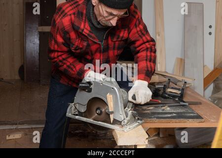 L'homme âgé travaille comme menuisier avec une scie circulaire dans son atelier. Vieillesse active Banque D'Images