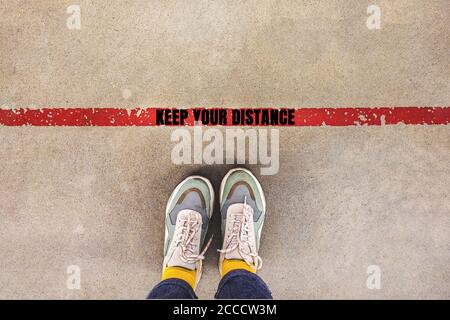 Personne debout sur la ligne rouge avec l'inscription GARDEZ VOTRE DISTANCE - social distance chantant, comme une nouvelle tendance de la vie normale. Concept de distance de sécurité Banque D'Images