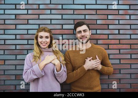 Gracieux gai positif jeune femme et homme ont des expressions satisfaites, garder les deux mains sur le coeur, se sentent reconnaissants aux invités, étant dans l'esprit élevé, St Banque D'Images