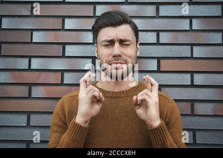 jeune homme beau se sentant nerveux et plein d'espoir, croisant les doigts, priant et espérant la bonne chance Banque D'Images