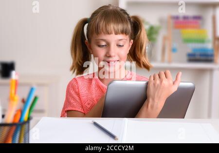 Bonne fille étudiant à la maison bureau de prendre des leçons à distance en utilisant une tablette Banque D'Images