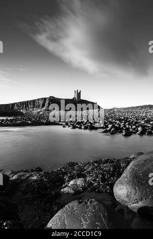 Le château de Dunstanburgh a tourné tôt le matin avec la mer du Nord qui s'est abatée dans la baie. Banque D'Images