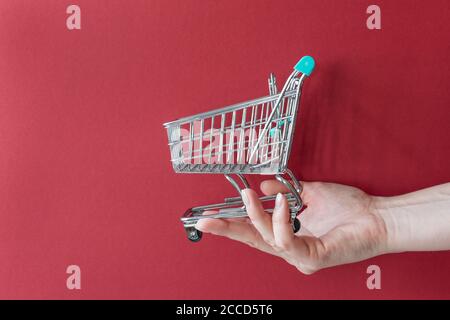 Main de femme avec un panier à jouets vide sur fond rouge. Concept commercial. Copier l'espace. Banque D'Images
