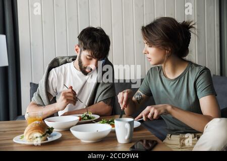 Charmant jeune couple ayant un petit déjeuner sain dans la cuisine, parlant Banque D'Images