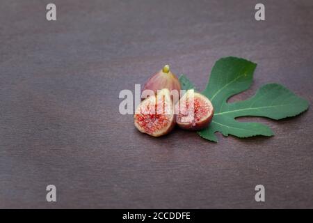 Deux figues sur une table en bois, une coupée en deux sur la feuille de figuier Banque D'Images