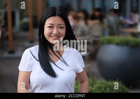 Une femme asiatique souriant et regardant l'appareil photo au café-terrasse. Arrière-plan flou Banque D'Images