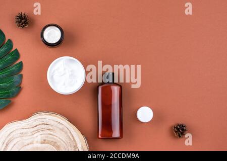 Cosmétiques naturels. Produits de soin du visage et du corps avec feuilles tropicales sur une surface brune. Masque hydratant pour le visage, pot à crème, bouteille de lotion Banque D'Images