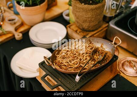 Gros plan d'une poêle à spaghetti sur un poêle en fonte dans une cuisine avec des assiettes blanches et des pots de fleurs. Banque D'Images
