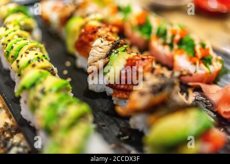 Sushis Rolls au restaurant. Sushis de luxe avec garniture d'avocat et d'anguille, maki arc-en-ciel, thon, tobiko, graines de sésame. Cuisine japonaise. Banque D'Images