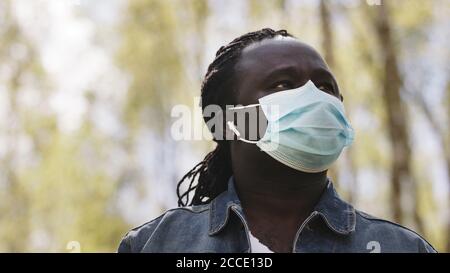 Portrait d'un homme africain avec masque médical et casque sans fil dans la nature. Photo de haute qualité Banque D'Images