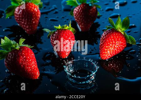 Fraises tombant sur une surface humide noire, éclats d'eau Banque D'Images