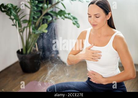 belle femme yogi caucasienne inspire le parfum des bâtons d'arôme, médite à la maison, assis sur le sol, se détendre Banque D'Images