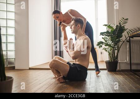 belle femme yogi enseigner à l'homme de faire des exercices, l'aider à prendre la bonne position, à l'intérieur. vue latérale Banque D'Images