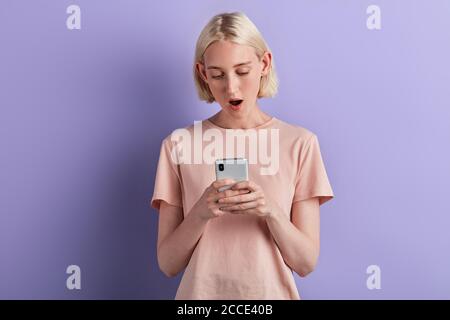 Jeune femme endormi fatiguée bâillonnant regarder les médias dans un téléphone mobile, surfer, naviguer sur le Net, gros plan portrait, isolé violet fond, studio sh Banque D'Images