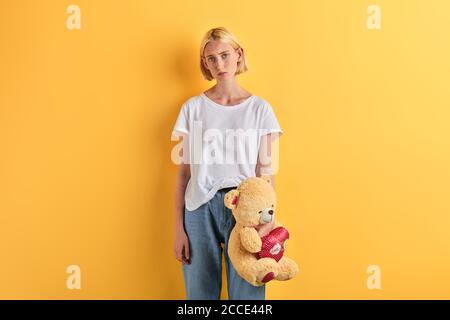 Fille dépressive en T-shirt blanc et jeans avec jouet dans les mains posant à l'appareil photo. Portrait gros plan, studio tourné, solitude, dépression Banque D'Images