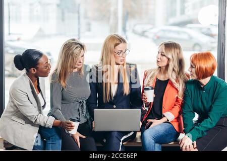 Société internationale d'affaires des femmes divers partenaires qui partagent leur expérience et les méthodes de travail, alors que la collecte avec ordinateur portable contre la fenêtre af Banque D'Images