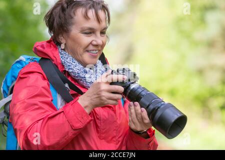 Portrait en gros plan d'une femme de randonnée avec appareil photo. Elle regarde le moniteur de la caméra. Banque D'Images