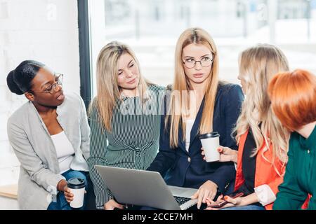 Société internationale d'affaires des femmes divers partenaires qui partagent leur expérience et les méthodes de travail, alors que la collecte avec ordinateur portable contre la fenêtre af Banque D'Images