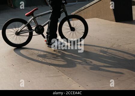 gros plan d'un jeune homme debout près de son vélo bmx ne montrant que ses jambes et de belles ombres sur le sol symbolisant la culture et le mode de vie des jeunes Banque D'Images