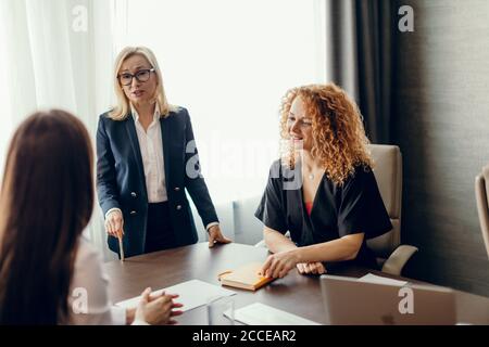 Des femmes experts en marketing assis autour de la table et regardant une femme orateur lors d'une réunion informelle. Femme blanche blonde exécutive donnant une présentation Banque D'Images