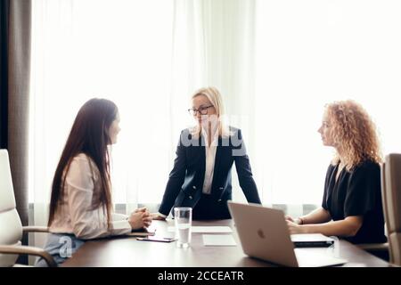 Des femmes experts en marketing assis autour de la table et regardant une femme orateur lors d'une réunion informelle. Femme blanche blonde exécutive donnant une présentation Banque D'Images