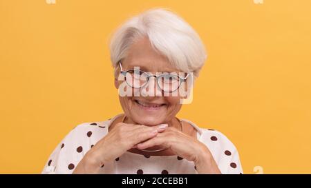 Femme âgée se reposant la tête sur ses mains et souriant. Isolé sur fond orange. Photo de haute qualité Banque D'Images