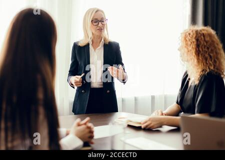 Des femmes experts en marketing assis autour de la table et regardant une femme orateur lors d'une réunion informelle. Femme blanche blonde exécutive donnant une présentation Banque D'Images