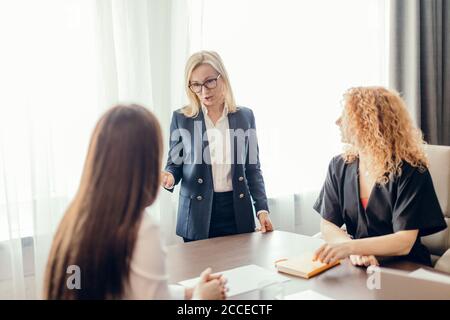 Les femmes d'affaires habillées avec élégance au bureau ayant des conversations et utilisant la technologie, se concentrent sur la femme blonde en train de dire quelque chose à ses collègues. Banque D'Images