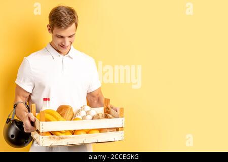 livraison express par jeune homme vigoureux souriant en t-shirt blanc isolé sur fond jaune. messagerie, concept de service de livraison Banque D'Images