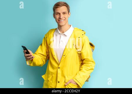 portrait d'un livreur de bonne apparence en uniforme jaune spécial, en utilisant un smartphone et en transportant des commandes dans un sac à dos pour les clients isolés sur le dos bleu Banque D'Images