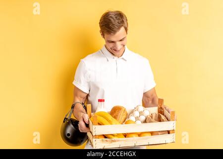 portrait d'un jeune messager transportant des aliments frais, des légumes et des fruits, portant un uniforme blanc avec un casque pour moto, concept de livraison express Banque D'Images