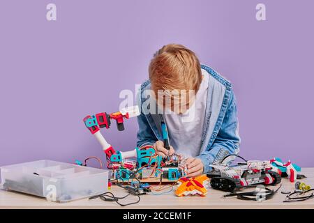 portrait d'un garçon blond soucieux d'assembler la robotique enfant garçon tenant des robots, la technique et essayant de les assembler en un. robots et enfants c Banque D'Images