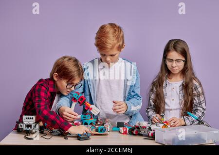 portrait d'enfants intelligents visant à faire un robot isolé en studio. les enfants caucasiens veulent être des ingénieurs et désireux de la robotique de l'enfance Banque D'Images