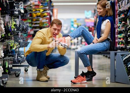 les jeunes clients caucasiens sont venus dans le magasin de vêtements de sport pour faire l'achat, le gars et la femme de beau s'impliquer dans divers sports, énorme. grand assortiment de g Banque D'Images